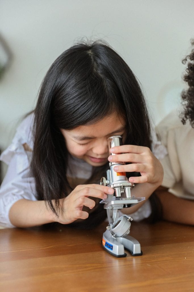 Photo: young girl peeking into a microscope